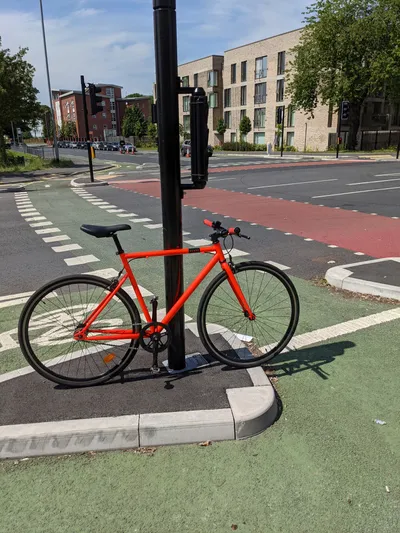 An orange fixed gear bicycle standing against a cycle only traffic light pole